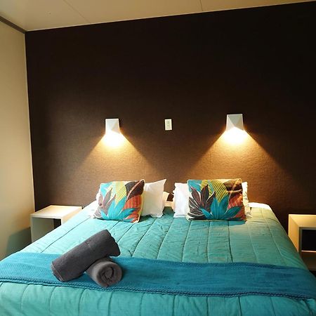 Taupo Debretts Spa Resort Экстерьер фото The image shows a bedroom with a modern and inviting layout. The focal point is a bed with a vibrant turquoise comforter, decorated with two colorful pillows featuring floral patterns. On either side of the bed, there are small nightstands with wall-