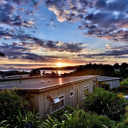 Taupo Debretts Spa Resort Экстерьер фото The photo depicts a serene landscape during sunset. In the foreground, there is a modest building partially covered by greenery. The roof of the building is visible, along with some windows. Surrounding the structure are lush plants and foliage. 

In
