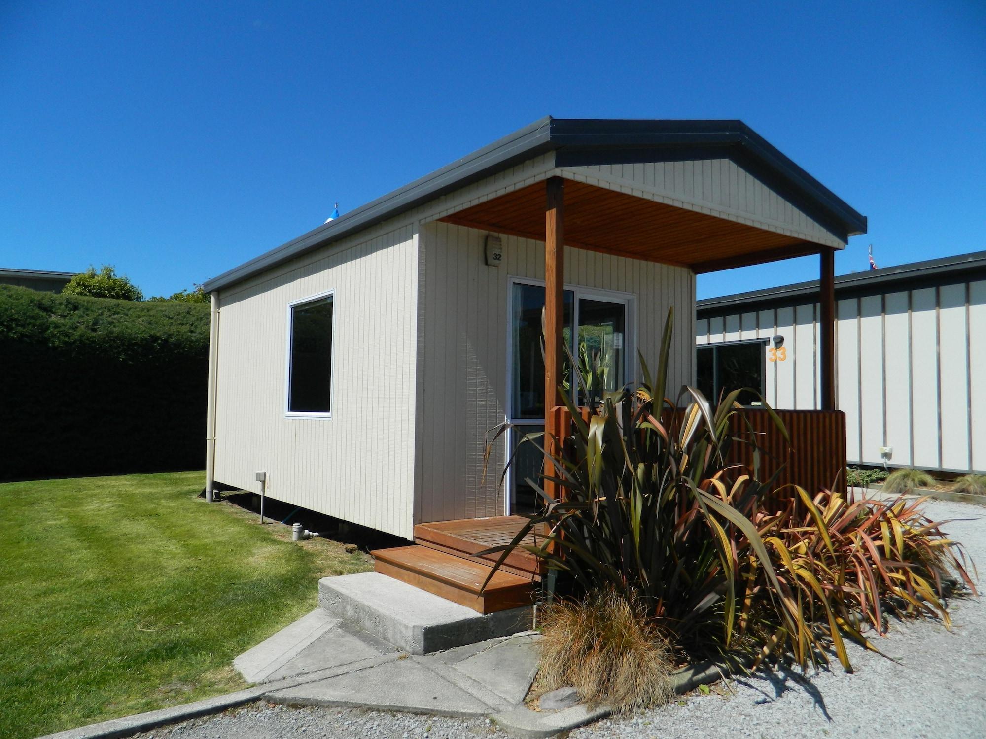 Taupo Debretts Spa Resort Экстерьер фото The photo shows a small, modern cabin or vacation home. It features a light-colored exterior with a a small porch at the entrance. The porch has wooden steps that lead up to the front door. Surrounding the cabin is a neat lawn, with some landscaping 