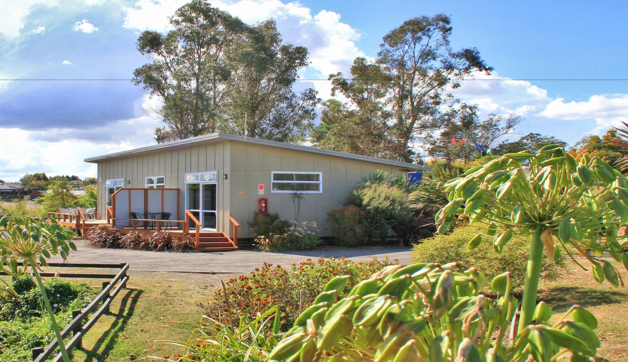 Taupo Debretts Spa Resort Экстерьер фото The image shows a small, modern building surrounded by greenery. The structure has a light-colored exterior with large windows and a ramp leading up to the entrance. In front of the building, there is a landscaped area with various plants and flowers