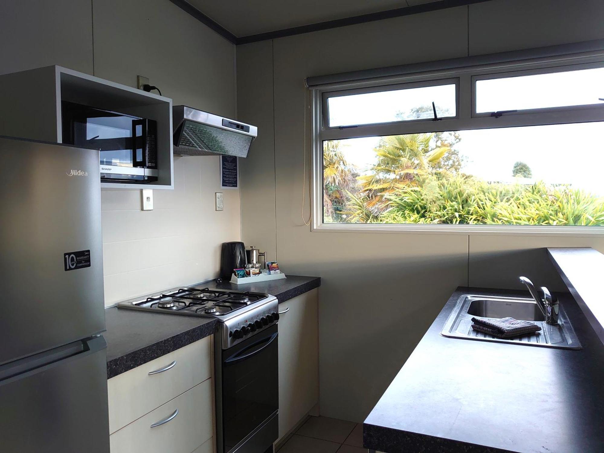Taupo Debretts Spa Resort Экстерьер фото The photo shows a kitchen equipped with modern appliances. On the left side, there is a refrigerator and a microwave above it. The kitchen features a gas stove with a range hood above. To the right, there is a kitchen sink with a countertop. A window