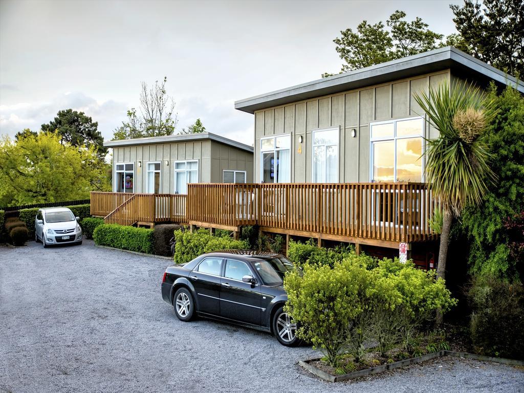 Taupo Debretts Spa Resort Экстерьер фото The photo shows two modern buildings, likely cabins or lodges, situated in a natural setting. They each have wooden decks in front and large windows. A few trees and plants surround the buildings, contributing to a lush environment. In the foreground