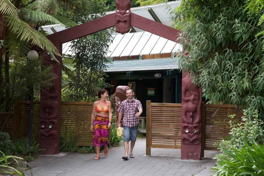 Taupo Debretts Spa Resort Экстерьер фото The photo depicts a welcoming entrance, marked by a decorative archway featuring traditional cultural carvings. Two individuals are walking through the entrance: one is a woman wearing a vibrant, patterned dress, and the other is a man dressed casual