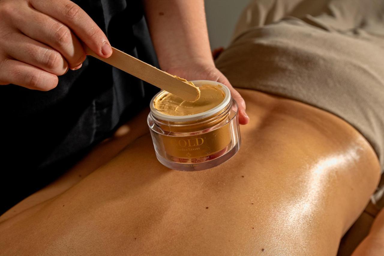 Taupo Debretts Spa Resort Экстерьер фото The photo shows a close-up of a back, likely during a spa or beauty treatment. A person is using a wooden spatula to apply a golden-colored substance from a jar to the skin. The jar is clear and labeled, and the skin appears smooth and slightly gloss