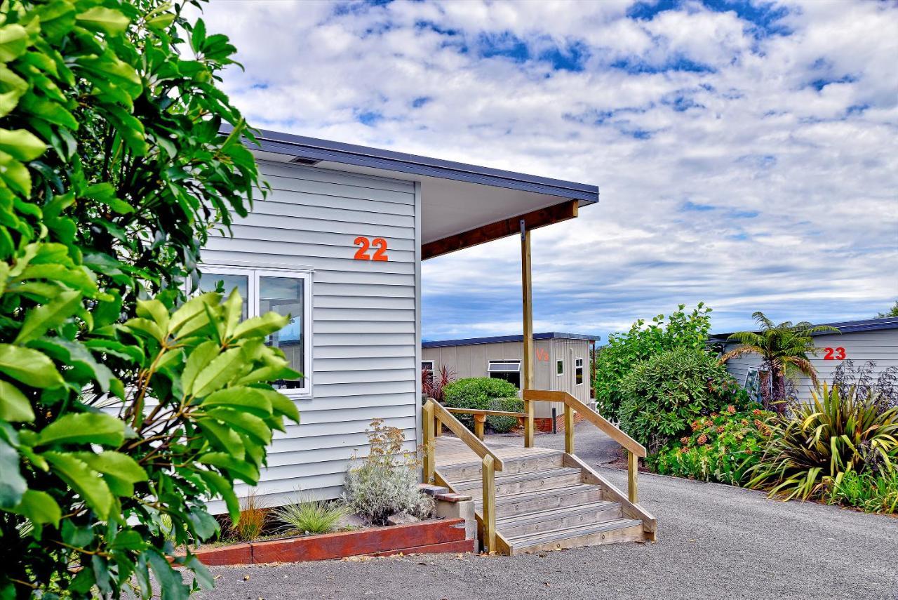 Taupo Debretts Spa Resort Экстерьер фото The photo shows a building, likely a cabin or cottage, with a wooden porch and stairs leading up to it. The structure has light-colored siding and the number "22" is prominently displayed on the side. Surrounding the building are various plants and t