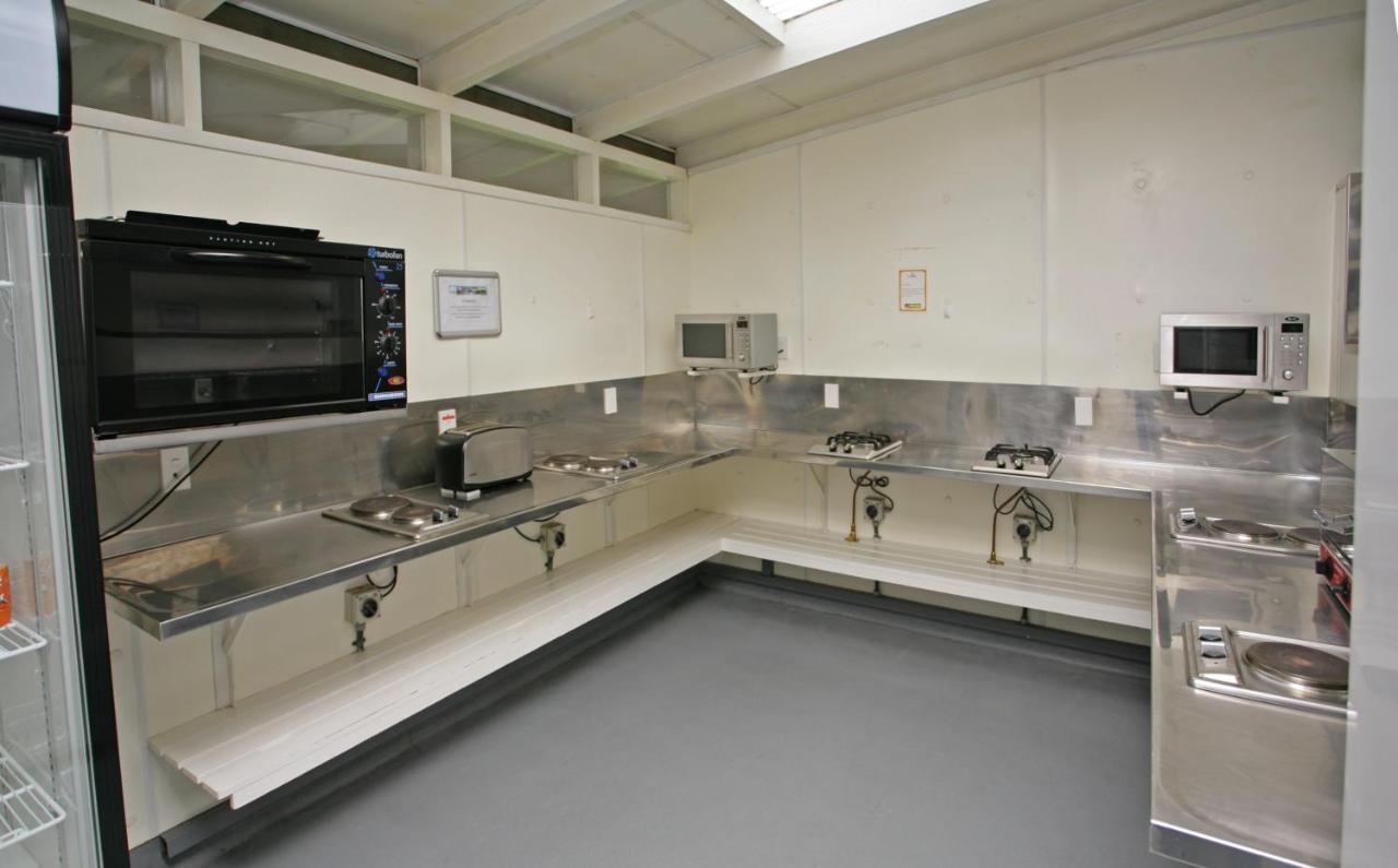 Taupo Debretts Spa Resort Экстерьер фото The photo shows a kitchen space that features stainless steel countertops and appliances. There is a wall-mounted microwave and another microwave placed on the counter. The kitchen is equipped with several gas burners and sinks. The floor has a smoot